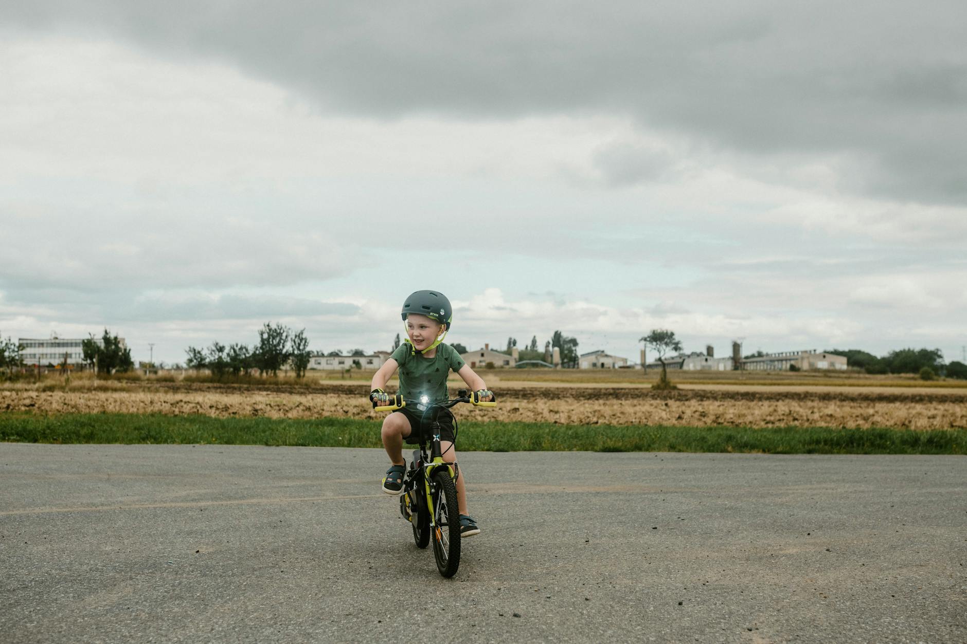 Young child riding a bicycle safely with a helmet in a rural setting.