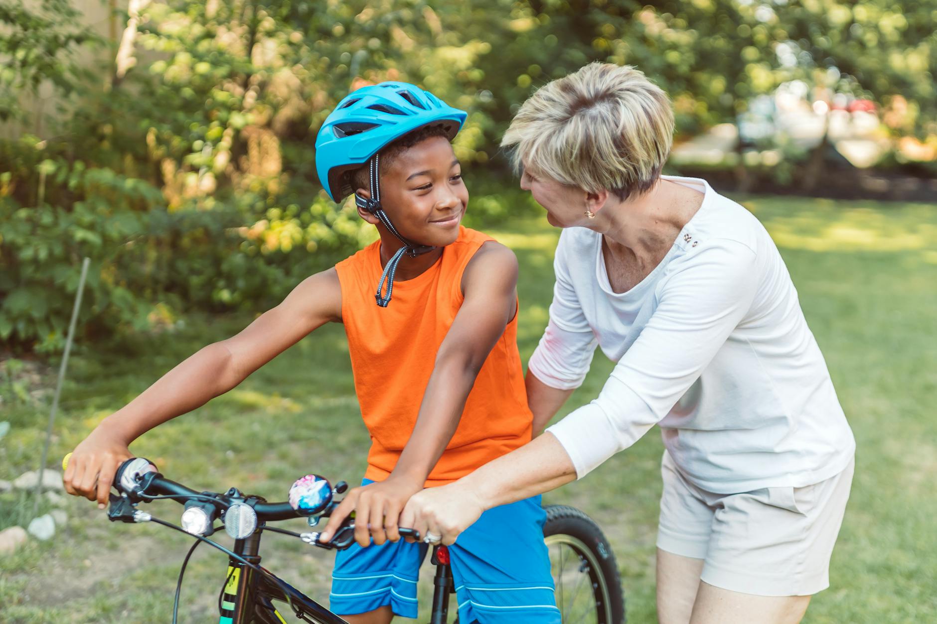 A joyful moment between a mother and son learning to ride a bike in a sunny park.