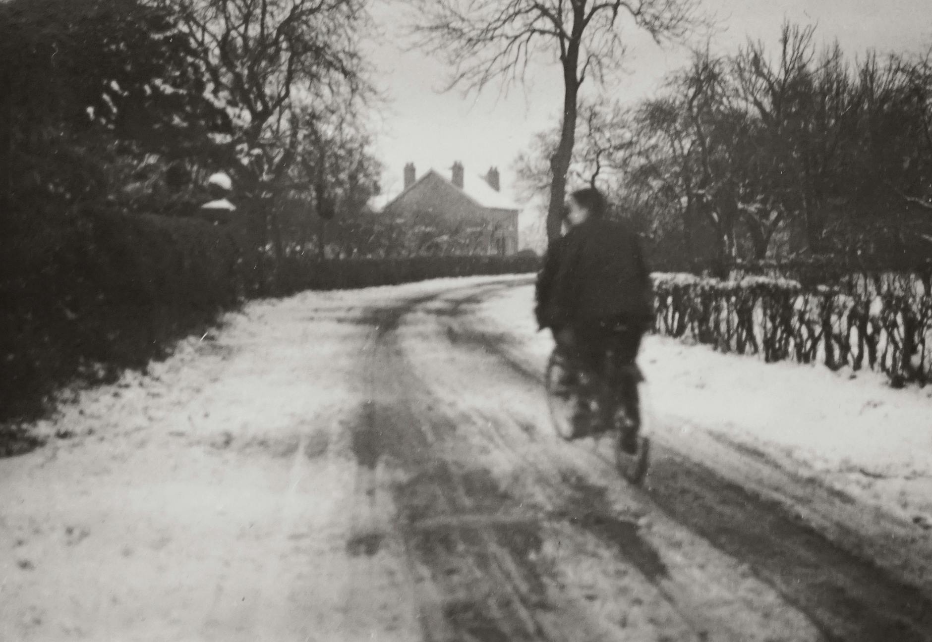 A cyclist rides on a snow-covered road capturing a vintage winter scene.