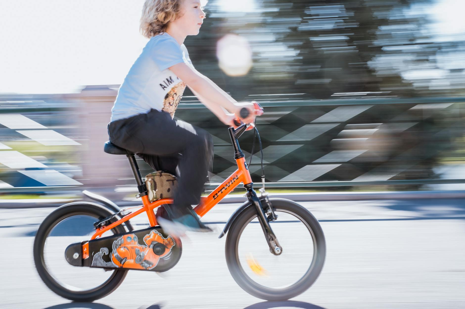 Young boy riding orange bicycle outdoors in Türkiye, showcasing motion and excitement.
