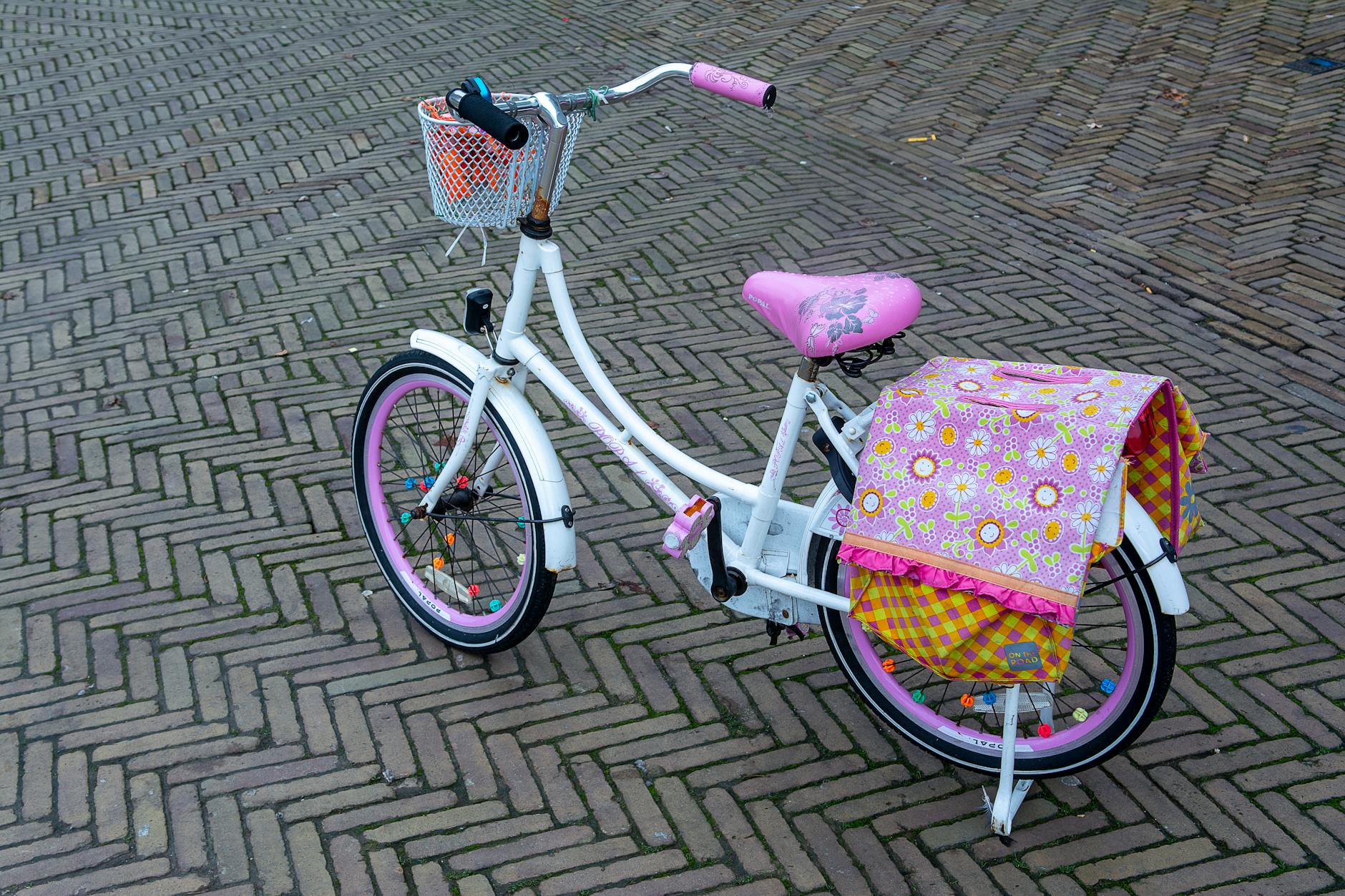 A charming pink child's bicycle with a floral bag parked on a patterned brick pavement.