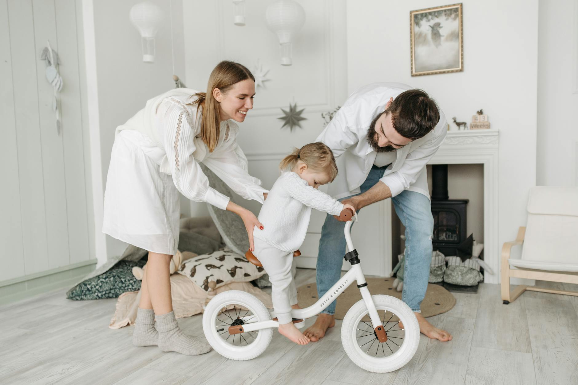 Parents assisting their child with a balance bike in a charming and cozy living room.