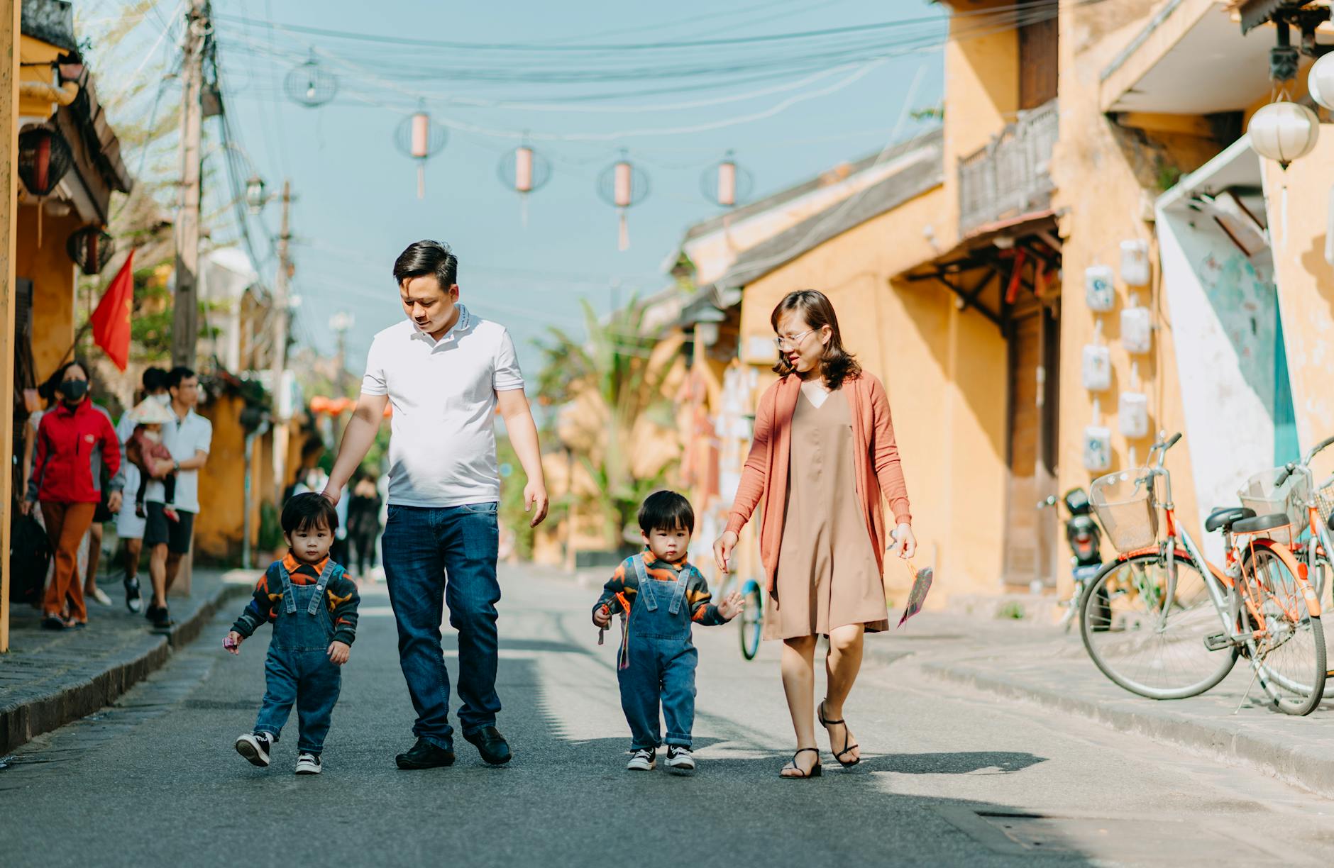 A family with young twins enjoy a sunny day walking down a vibrant street.