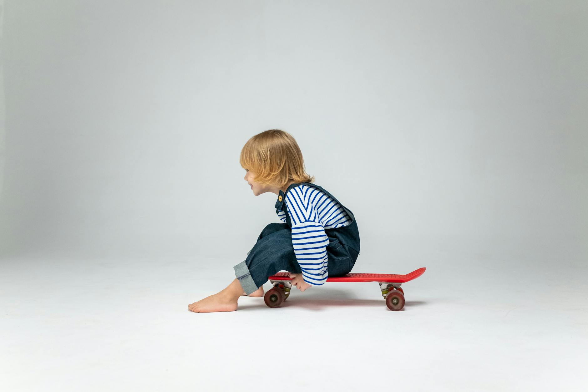 A young child balances playfully on a skateboard in a bright studio setting, exuding joy and energy.