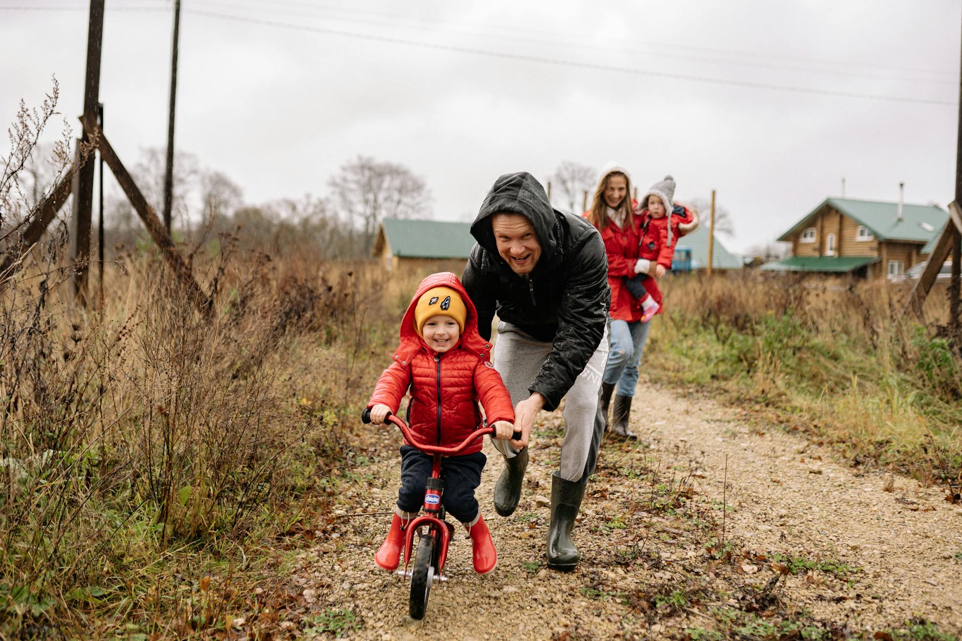 A happy family enjoys a bonding moment outdoors with a child learning to ride a bicycle on a fall day.
