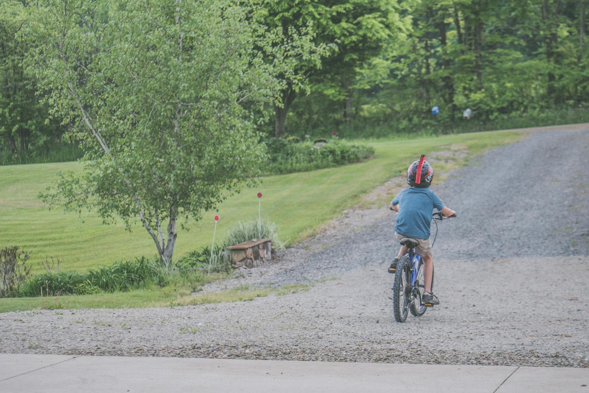 A young child riding a bicycle on a gravel path surrounded by lush greenery and trees.