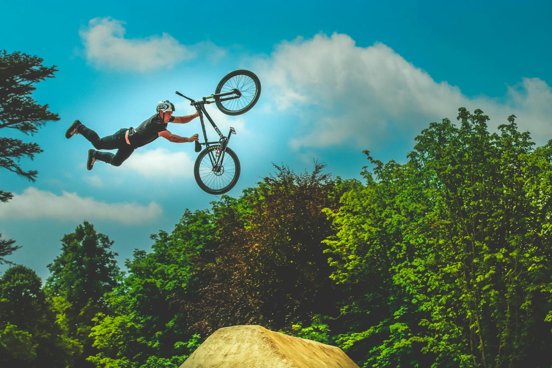 A BMX rider performs an incredible aerial trick against a vibrant park backdrop on a sunny day.