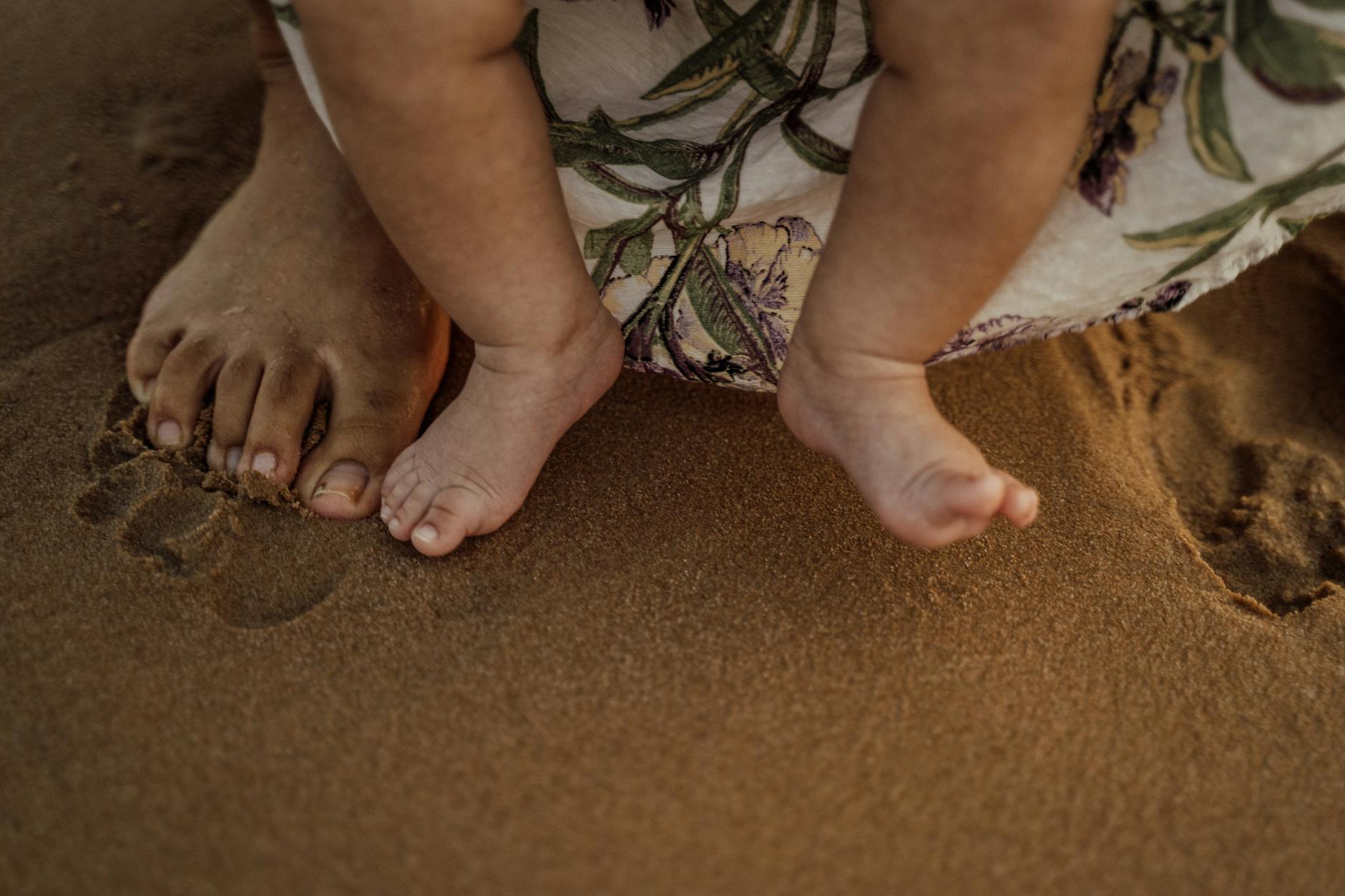 Close-up of mother and baby feet touching sand, showcasing a tender family moment.