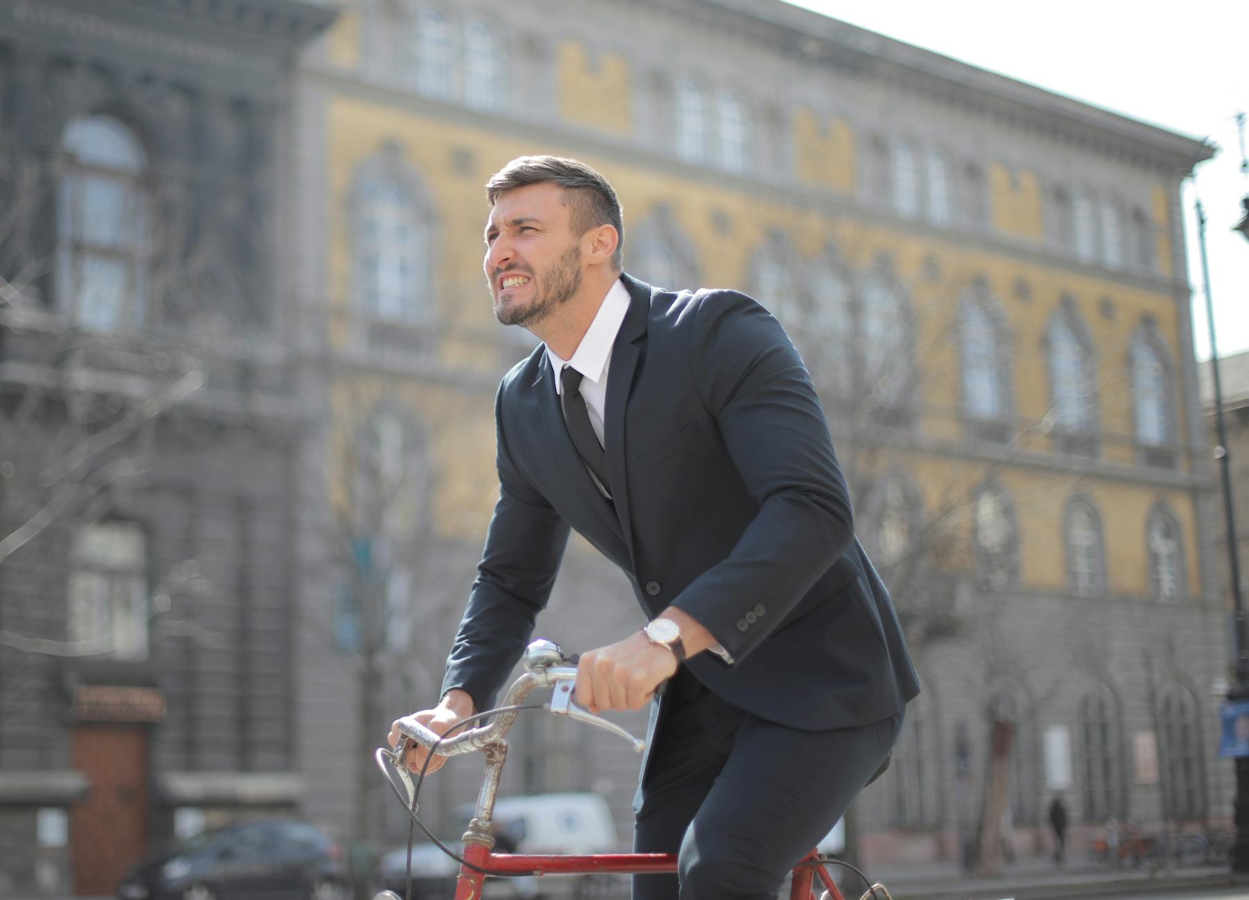 Man in formal attire cycling through a city street during the day.