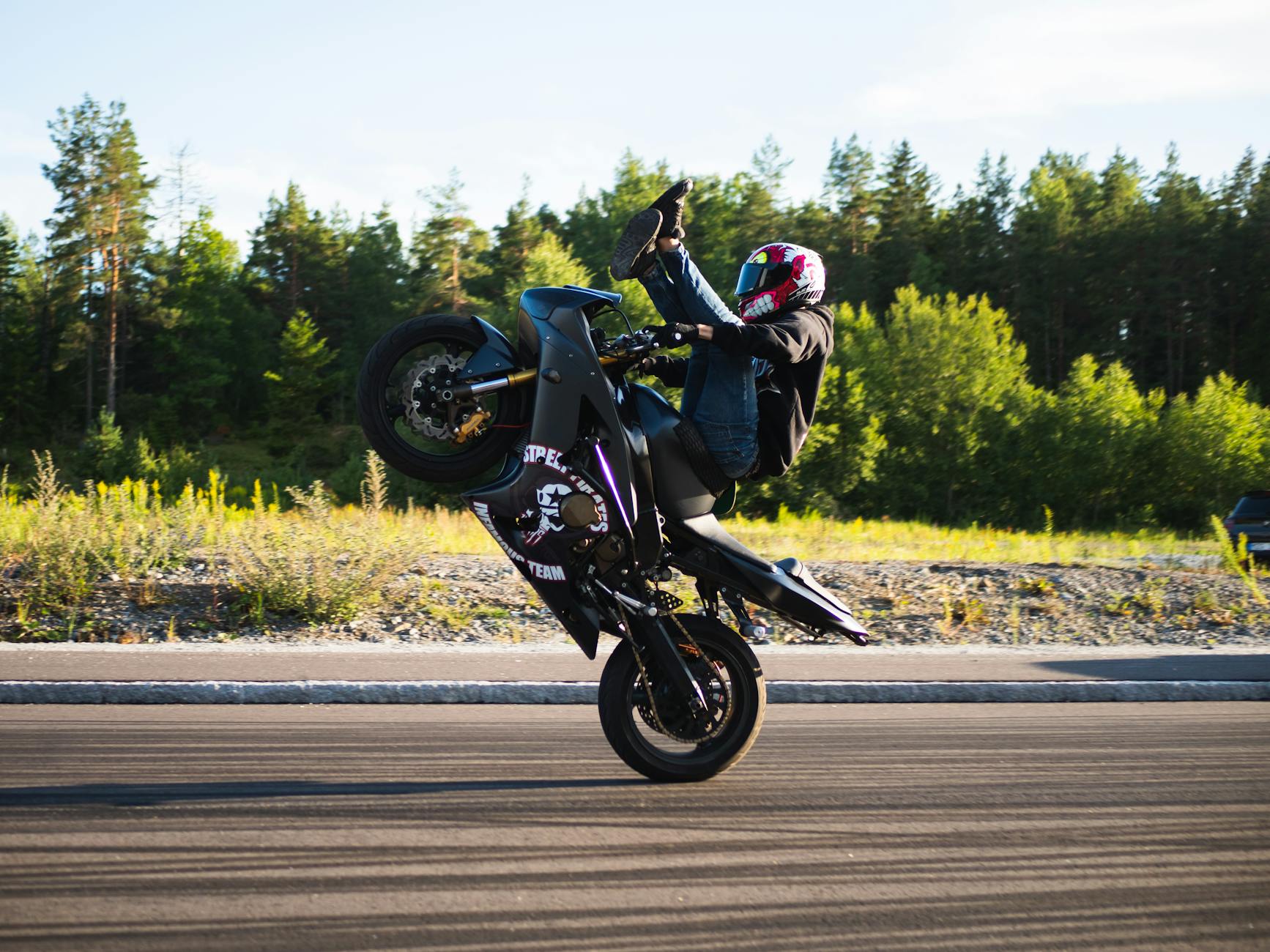A daring motorcycle stunt rider executes a wheelie on a sunny day in Sweden, capturing the thrill of adventure.