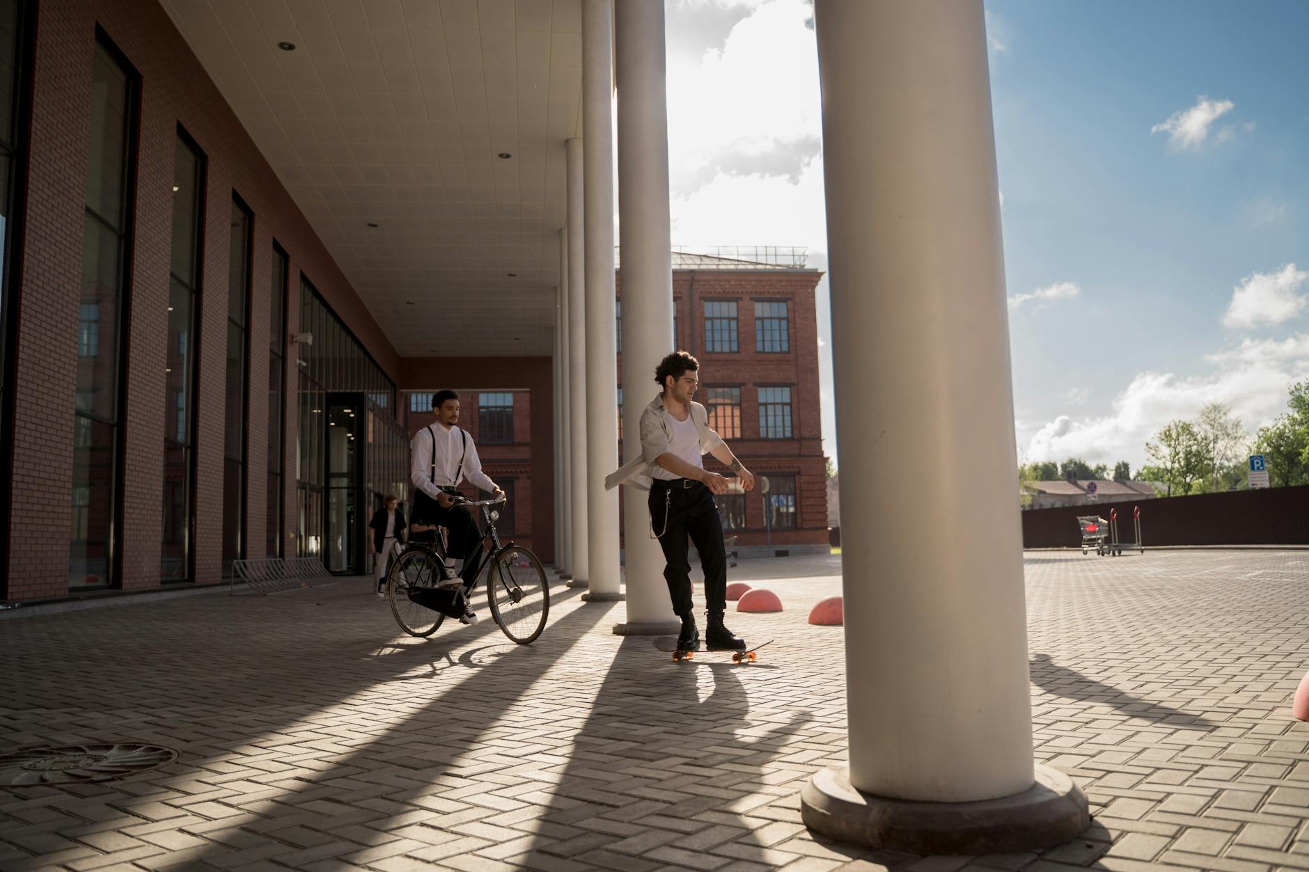 Two men enjoy skateboarding and biking in a modern urban environment on a sunny day.
