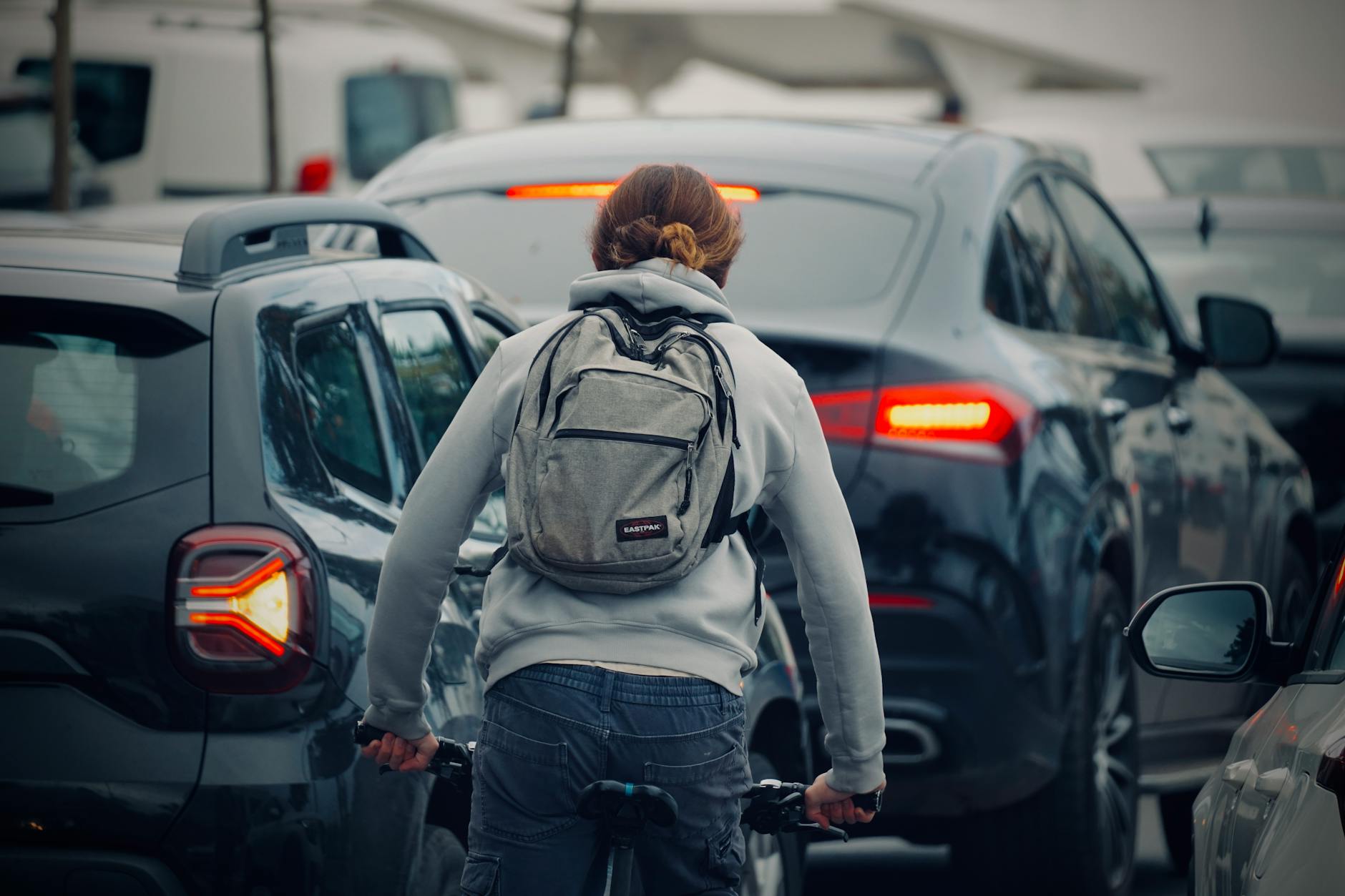 A cyclist wearing a backpack rides through a congested city traffic jam during daytime.
