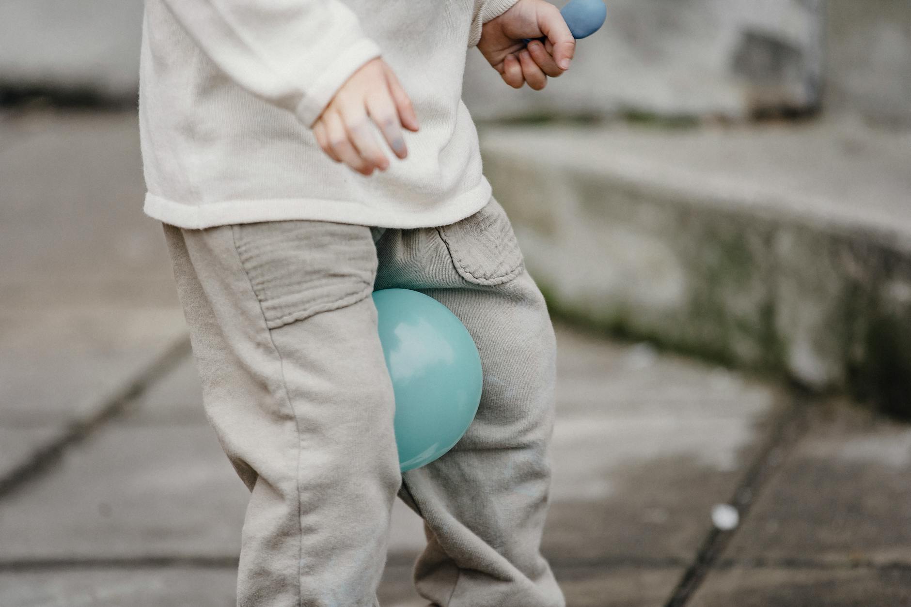 A child casually playing with a balloon on a pavement outside, enjoying free time.