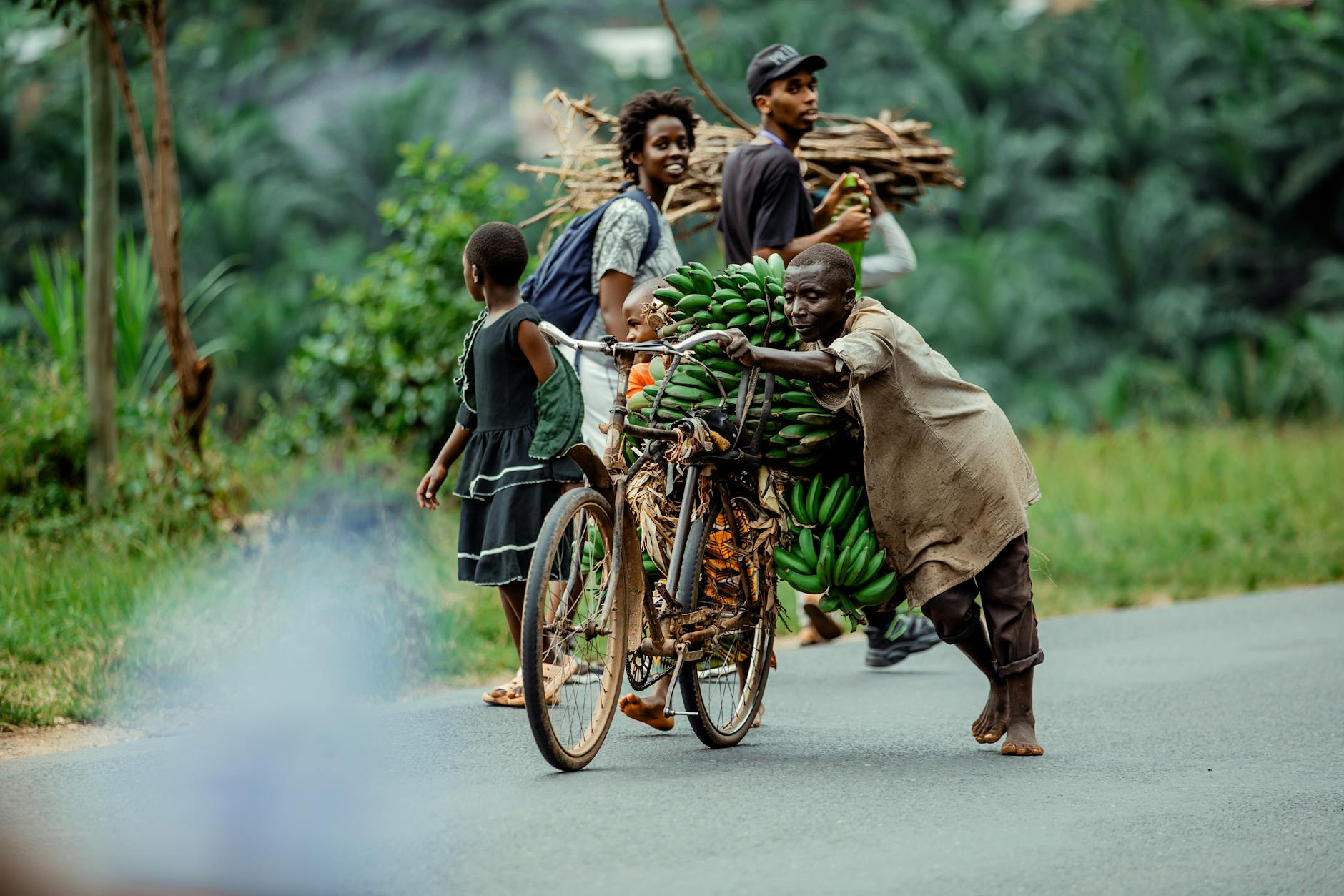 African villagers transport bananas and firewood on a rural road, showcasing daily life.