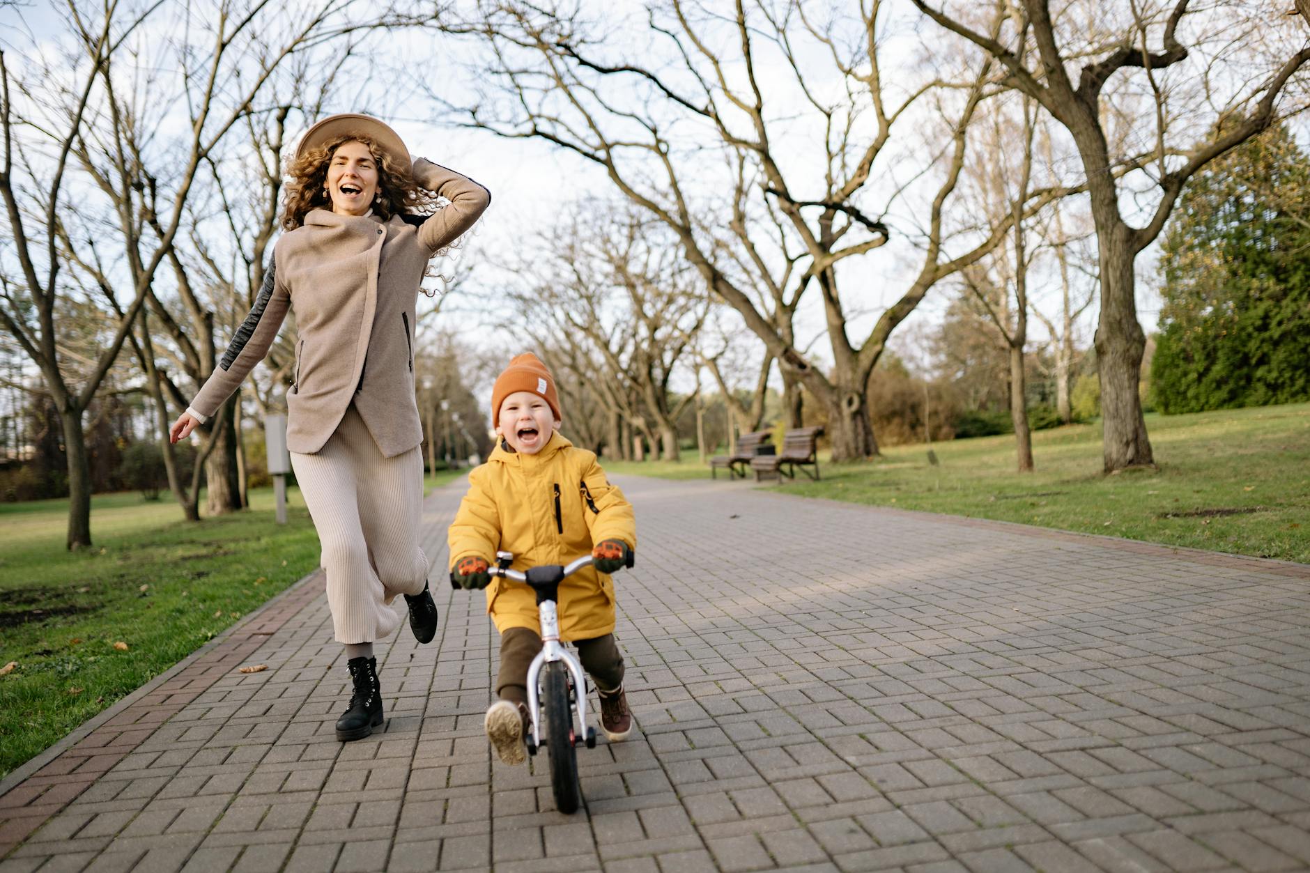 Mother and son riding a balance bike and running joyfully in a park on an autumn day.